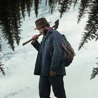 Joel Edgerton como Robert Griner com um machado na neve em cena do filme Sonhos de Trem (2024)