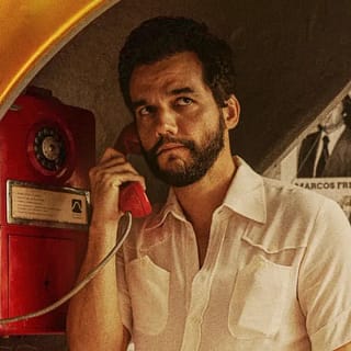 Wagner Moura em cena do filme O Agente Secreto usando um orelhão durante a ditadura militar no Brasil